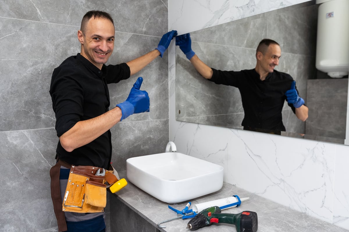 The worker installs the mirror in the bathroom. High quality photo