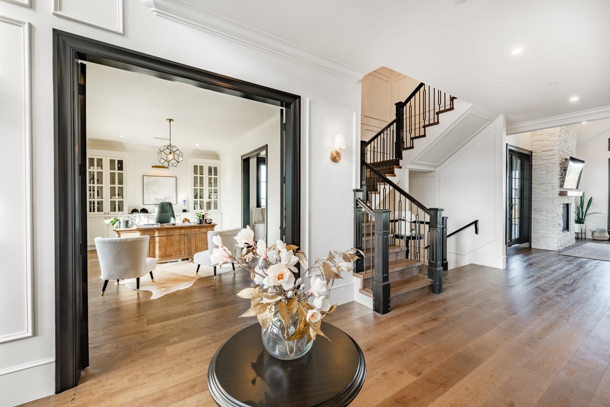 Beautiful large and luxurious estate home interior front door entry hallway foyer with large glass and black wood door expansive entry with a round table containing an arrangement of dried flowers in a bouquet.