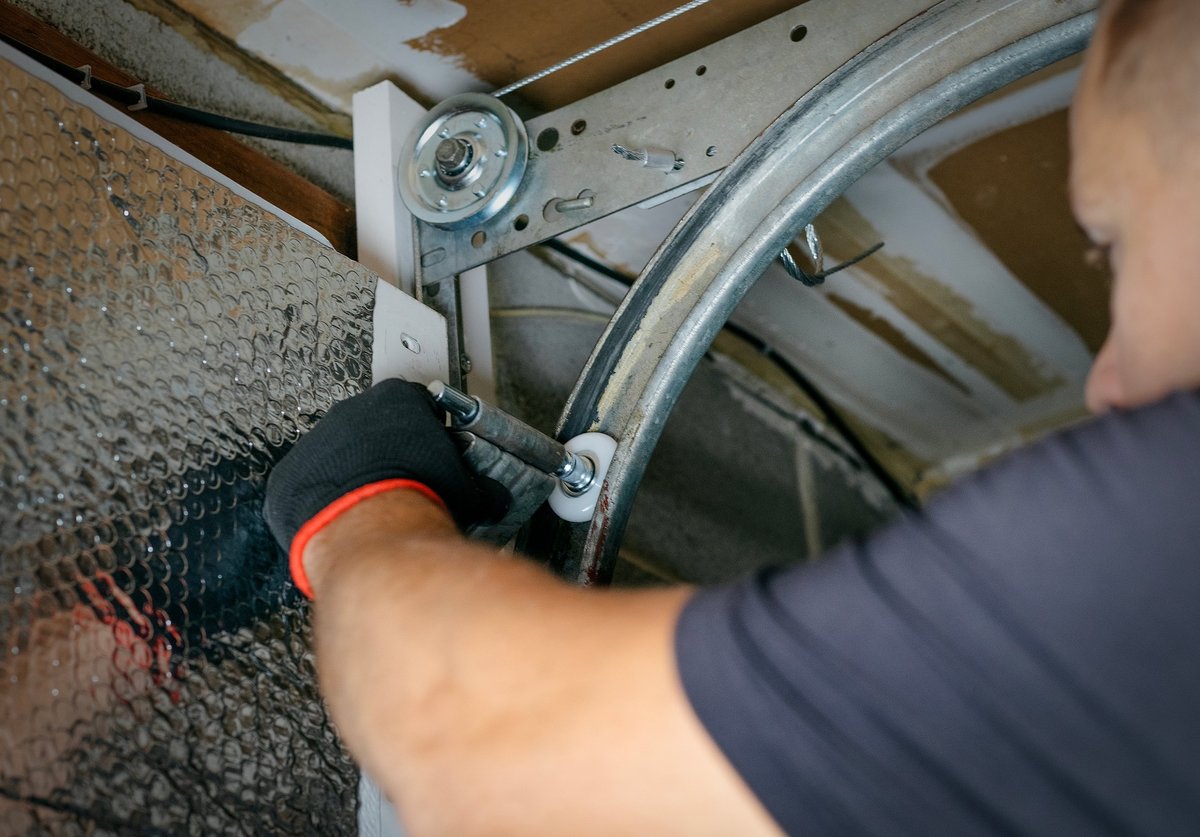 Adult man professionally and attentively repairing a garage door with tools, demonstrating focus and craftsmanship