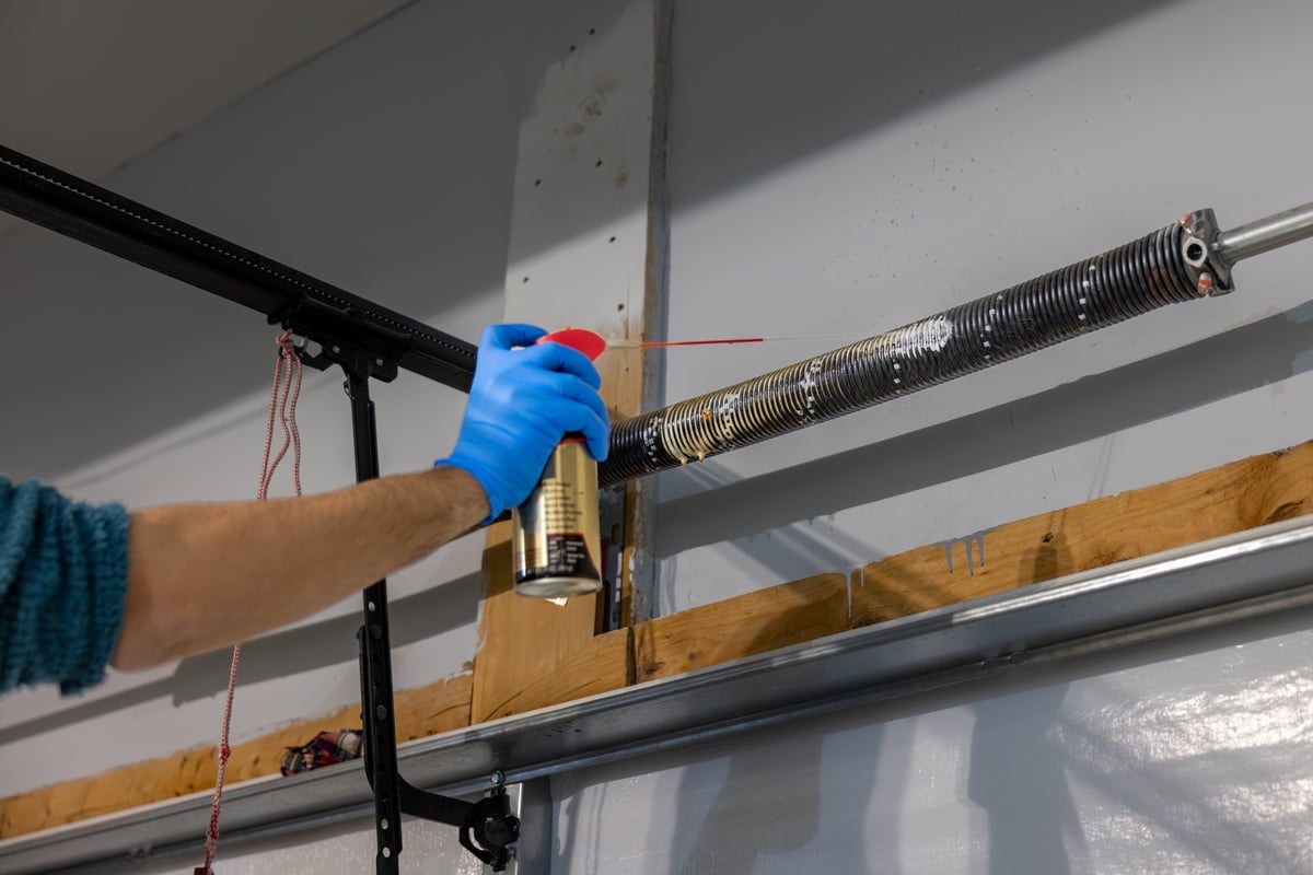 Man applies maintenance oil and lubricant to coiled torsion spring for garage door in order to keep the spring from rusting and becoming noisy